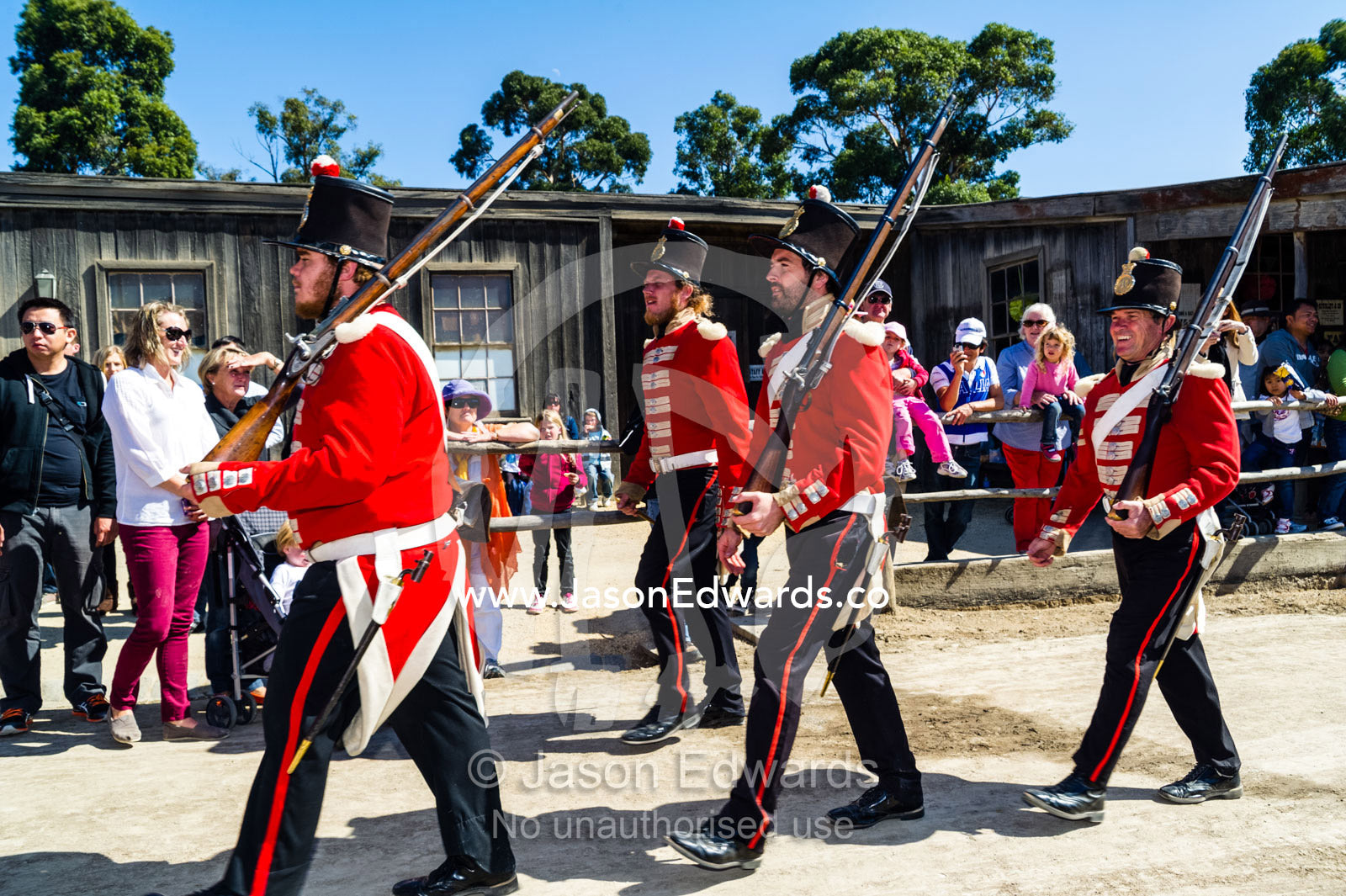 A patrol of British Redcoat soldiers march in formation past tourists in a gold mine town museum. Sovereign Hill, Ballarat, Victoria, Australia.