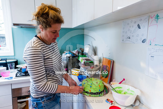 A mother decorating a birthday cake in the kitchen. Carlton North, Melbourne, Victoria, Australia.