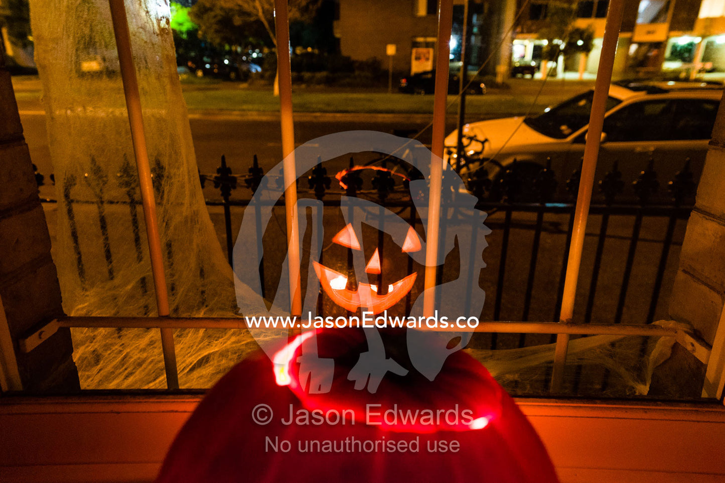 The fiery eyes and grin of a jack-o-lantern pumpkin in a house window on Halloween. Carlton North, Melbourne, Victoria, Australia.