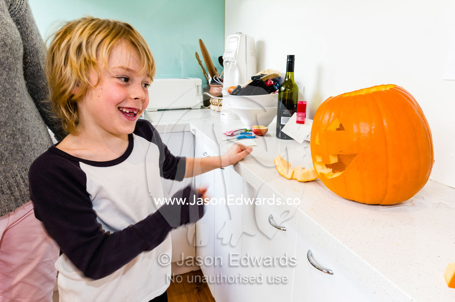 A boy gives a toothy smile whilst making a jack-o-lantern pumpkin in a kitchen for Halloween. Carlton North, Melbourne, Victoria, Australia.