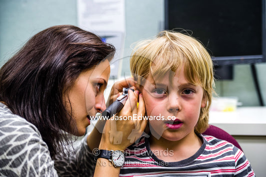 An audiologist examines a boys ears and performs hearing tests in a clinic. The University of Melbourne Audiology Clinic, Carlton, Melbourne, Victoria, Australia.