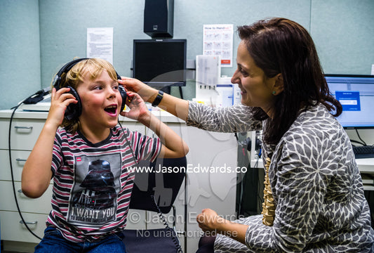 An audiologist examines a boys ears and performs hearing tests in a clinic. The University of Melbourne Audiology Clinic, Carlton, Melbourne, Victoria, Australia.