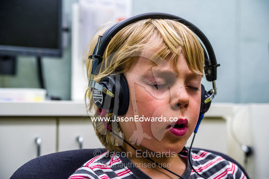 A boy concentrating whilst he listens for sounds in headphones during a hearing test in an audiologist clinic. The University of Melbourne Audiology Clinic, Carlton, Melbourne, Victoria, Australia.