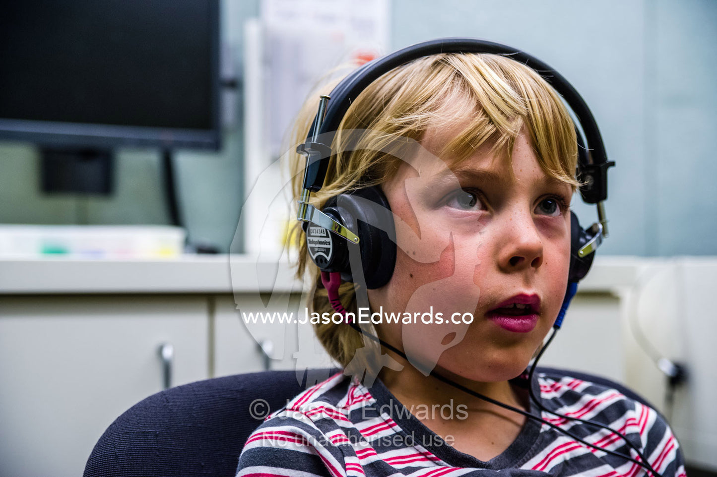 A boy concentrating whilst he listens for sounds in headphones during a hearing test in an audiologist clinic. The University of Melbourne Audiology Clinic, Carlton, Melbourne, Victoria, Australia.