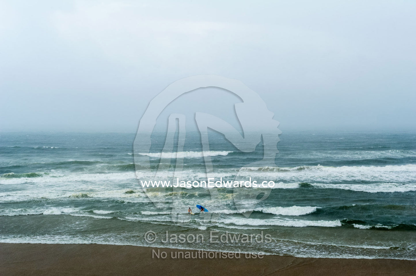 A pair of women go surfing in a rugged and stormy ocean. Coolum Beach, Queensland, Australia.