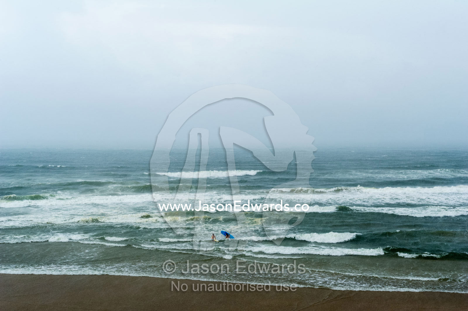 A pair of women go surfing in a rugged and stormy ocean. Coolum Beach, Queensland, Australia.