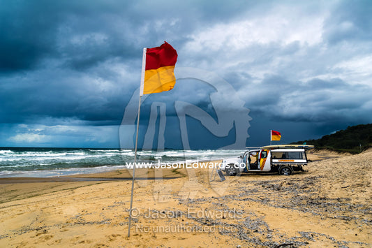 The red and yellow flag and 4wd of a lifeguard patrol on a stormy beach. Yaroomba Beach, Queensland, Australia.