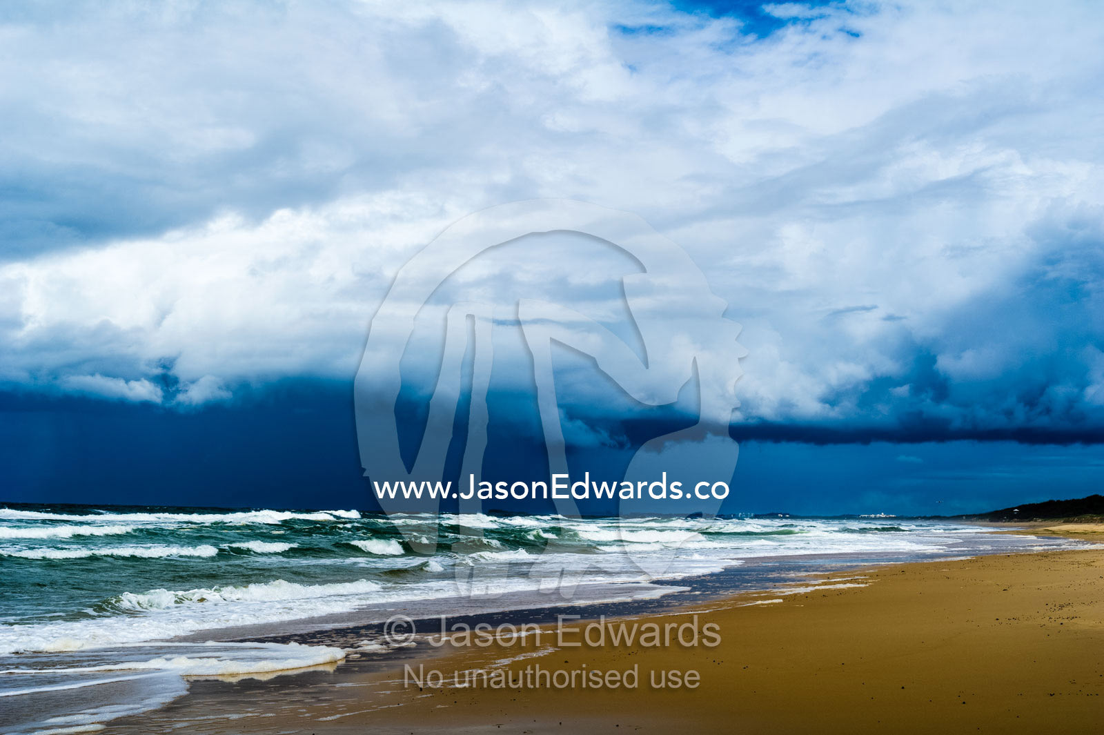 Ominous black storm clouds roll in over waves rolling onto an empty beach. Yaroomba Beach, Queensland, Australia.