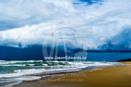 Ominous black storm clouds roll in over waves rolling onto an empty beach. Yaroomba Beach, Queensland, Australia.