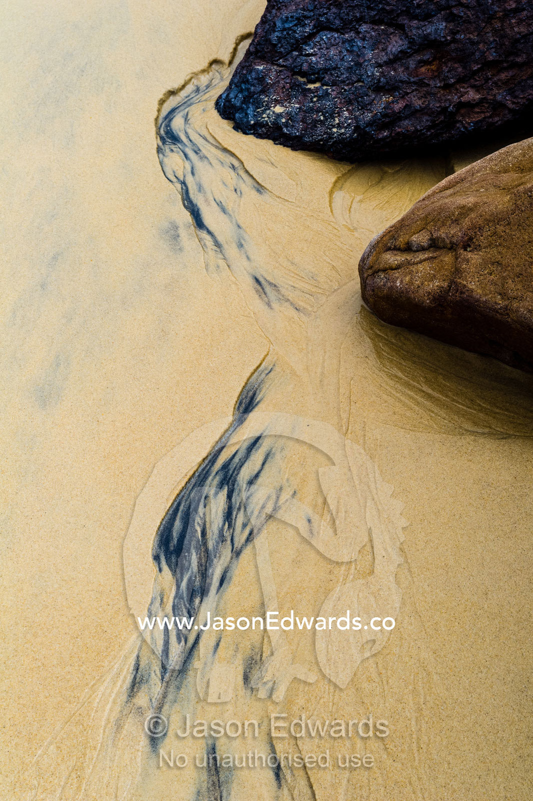 Water trickles around rocks on a sandy beach at low tide. Point Arkwright, Yaroomba Beach, Queensland, Australia.