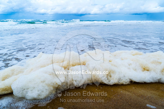 Foam generated by storm surge waves rolls onto an empty beach. Point Arkwright, Yaroomba Beach, Queensland, Australia.