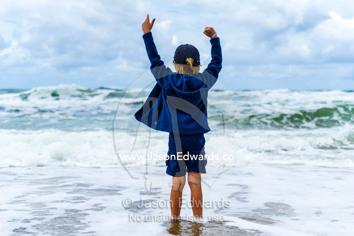 A boy playing in the shallows as storm surge waves roll onto an empty beach. Point Arkwright, Yaroomba Beach, Queensland, Australia.