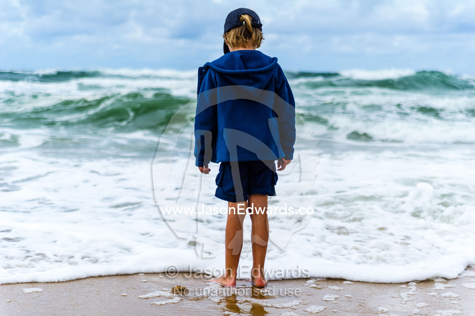 A boy playing in the shallows as storm surge waves roll onto an empty beach. Point Arkwright, Yaroomba Beach, Queensland, Australia.
