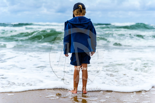 A boy playing in the shallows as storm surge waves roll onto an empty beach. Point Arkwright, Yaroomba Beach, Queensland, Australia.