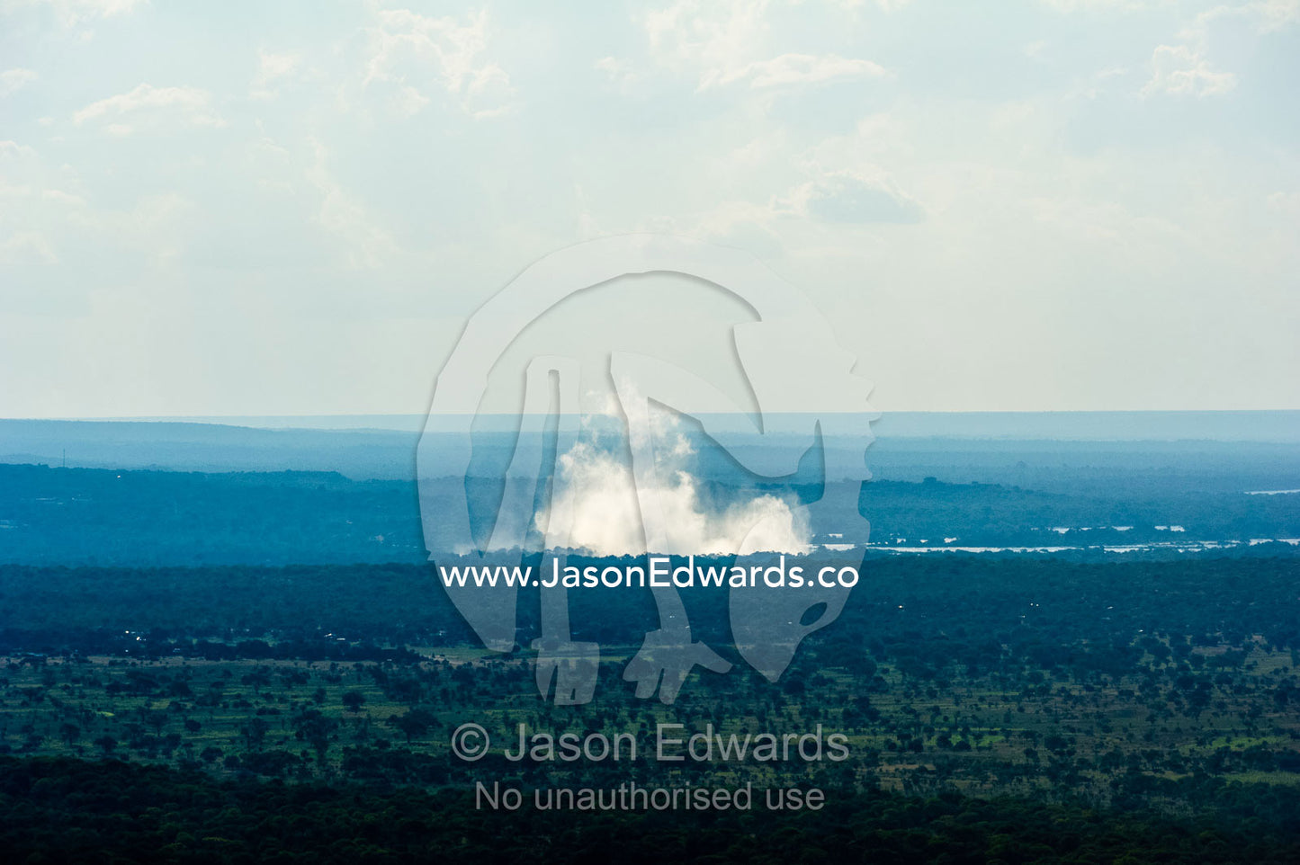 Mist rises from Victoria Falls over a vast flat plain. Victoria Falls, Mosi-oa-Tunya National Park, Zambia.