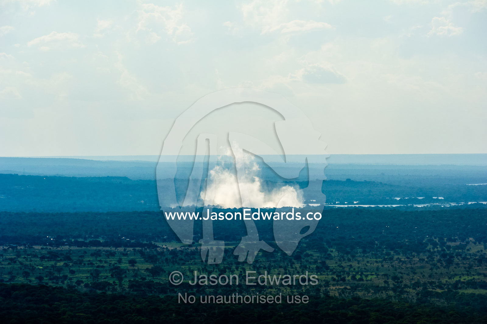 Mist rises from Victoria Falls over a vast flat plain. Victoria Falls, Mosi-oa-Tunya National Park, Zambia.