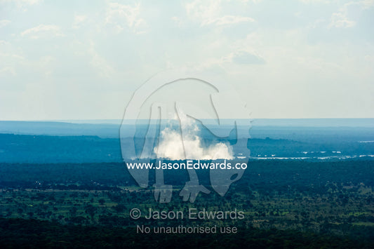 Mist rises from Victoria Falls over a vast flat plain. Victoria Falls, Mosi-oa-Tunya National Park, Zambia.