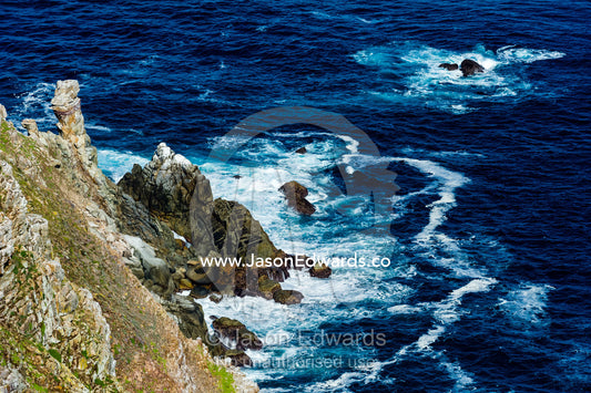 Wave foam trapped in currents along the base of steep jagged coastal cliffs. Cape of Good Hope, Cape Point, Table Mountain National Park, Cape Peninsula, South Africa.