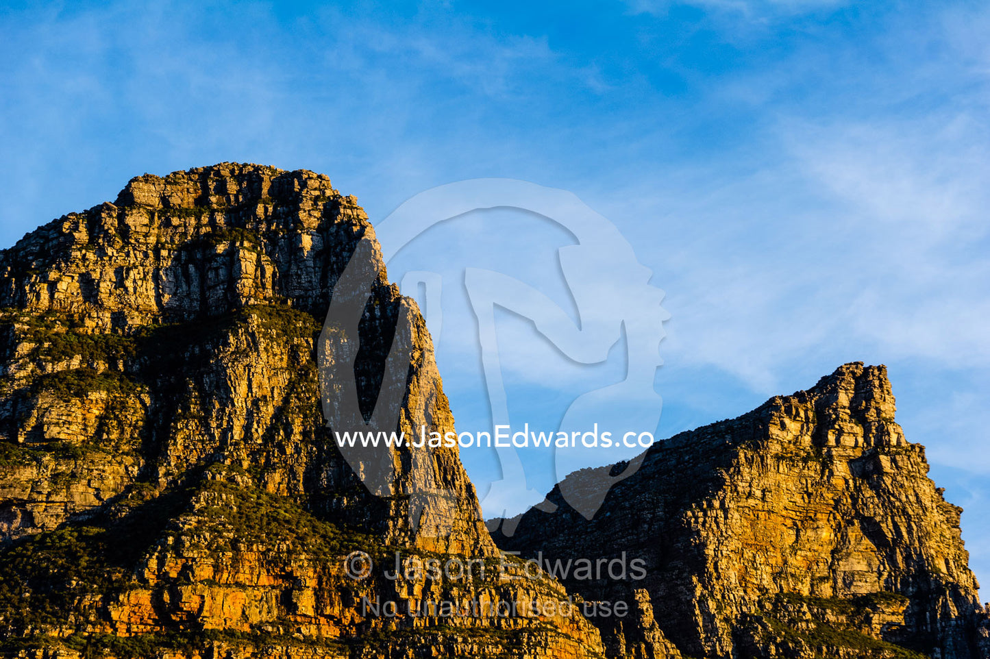 Jagged mountain peaks and cliffs catch the last rays of the setting sun. The Twelve Apostles, Chapmans Peak Mountain Range, Cape Town, Western Cape, South Africa.