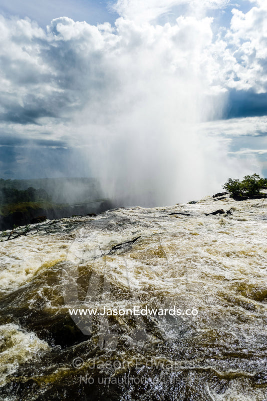 The rapids of the Zambezi River tumble over Victoria Falls sending up a plume of mist. Zambezi River, Victoria Falls, Mosi-oa-Tunya National Park, Zambia.
