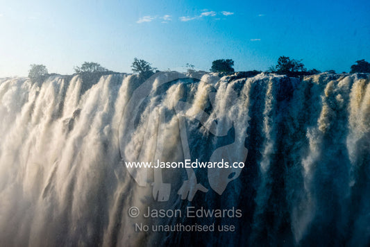 Sunlight catches the cascading pillars of the Zambezi River as they pour over Victoria Falls. Zambezi River, Victoria Falls, Mosi-oa-Tunya National Park, Zambia.