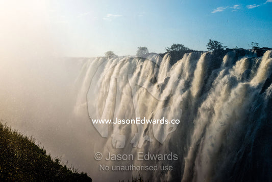 Sunlight catches the cascading pillars of the Zambezi River as they pour over Victoria Falls. Zambezi River, Victoria Falls, Mosi-oa-Tunya National Park, Zambia.
