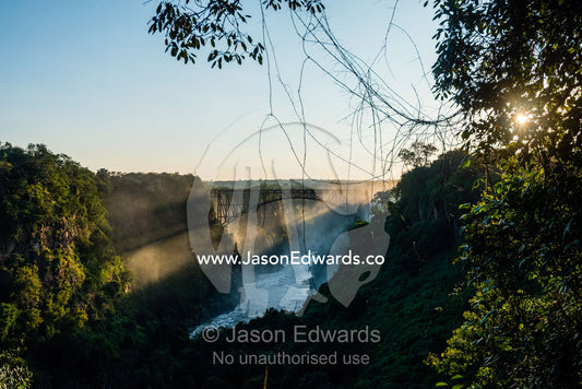 Sun rays pierce a misty gorge above the Zambezi River. Zambezi River, Victoria Falls, Mosi-oa-Tunya National Park, Zambia.