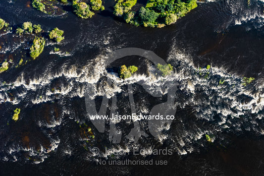 An aerial view of rapids as the Zambezi River rounds an island. Zambezi River, Victoria Falls, Mosi-oa-Tunya National Park, Zambia.