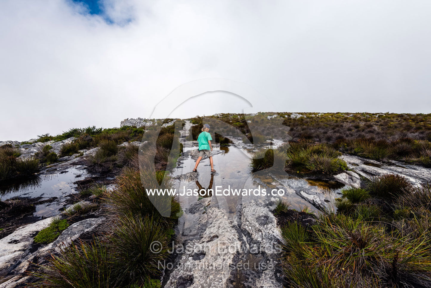 A boy leaps across pools of water captured in rock holes on the summit of Table Mountain. Table Mountain, Cape Town, Western Cape, South Africa.