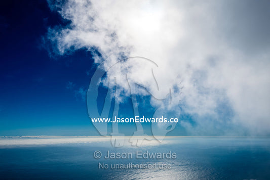 A cloud bank descending over calm blue ocean. Table Bay, Cape Town, Western Cape, South Africa.