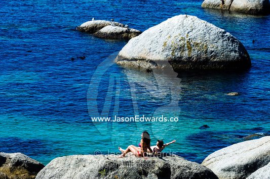 A couple sunbathing on a boulder above a clear blue sea. Boulders Beach, Cape Peninsula, Cape Town, Western Cape Province, South Africa.