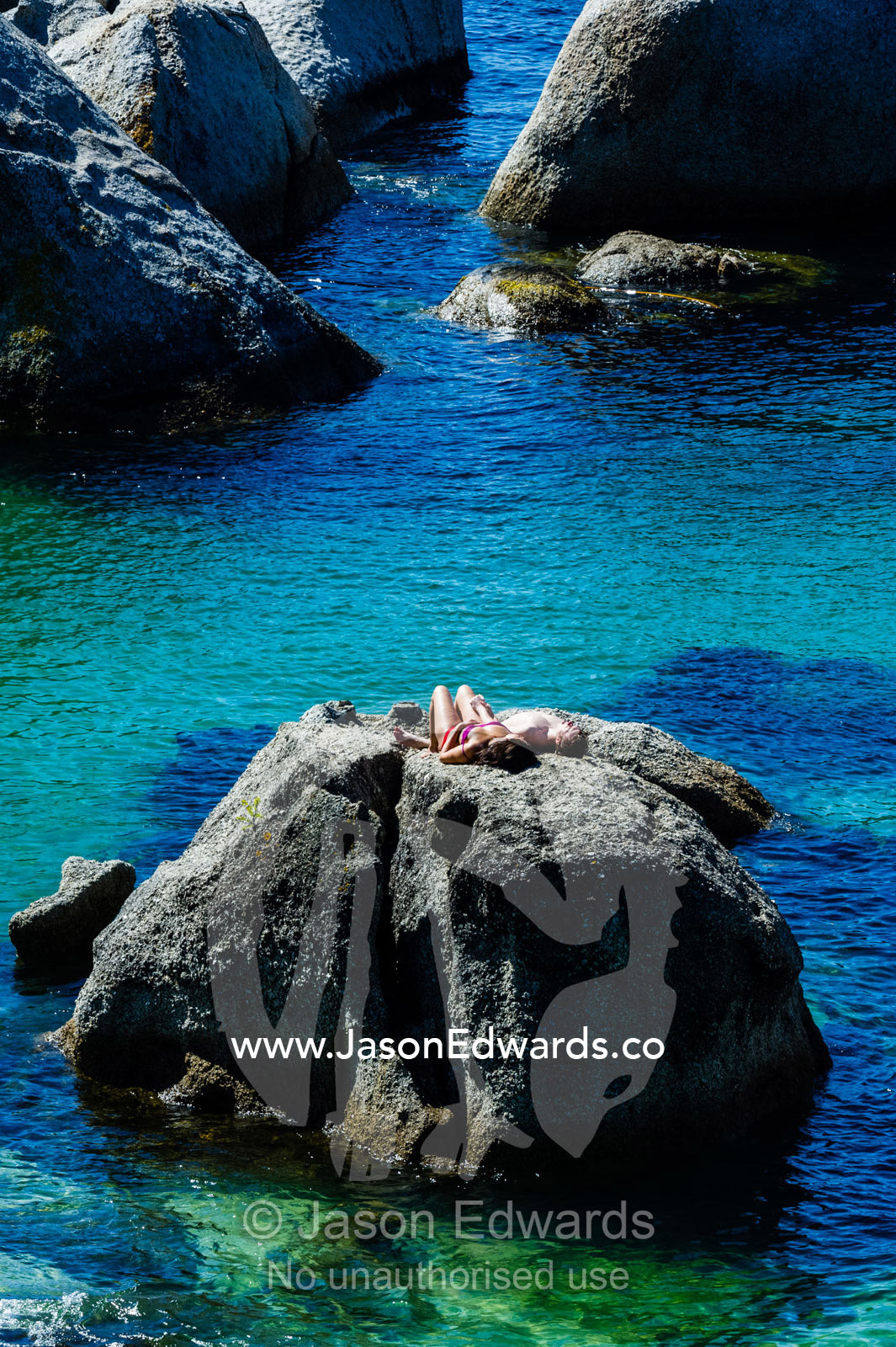 A couple sunbathing on a boulder above a clear blue sea. Boulders Beach, Cape Peninsula, Cape Town, Western Cape Province, South Africa.