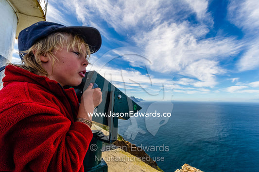 A boy searching the ocean through coin operated binoculars on a lighthouse. Cape of Good Hope, Cape Point, Table Mountain National Park, Cape Peninsula, South Africa.