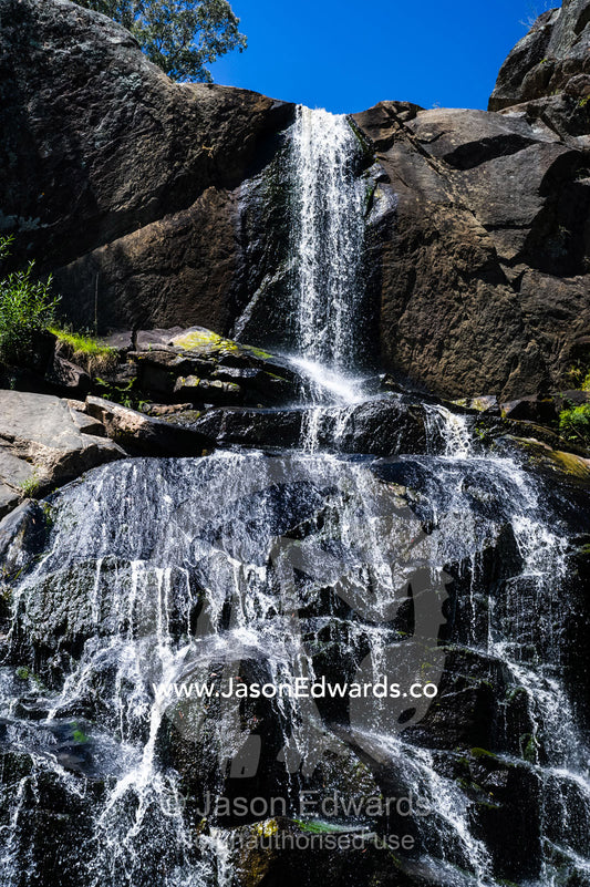A stream cascades in a waterfall over boulders into a forest pool. Faithfuls Creek Waterfall, Euroa, Strathbogie, Victoria, Australia.