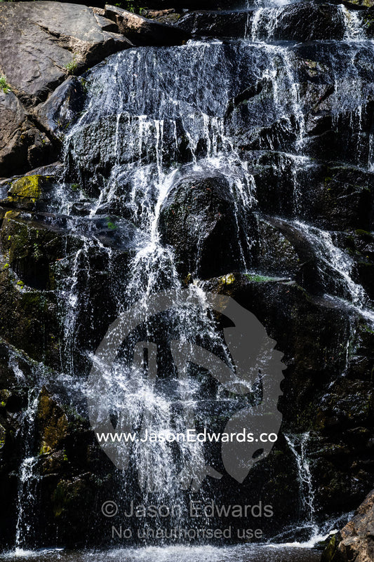 A stream cascades in a waterfall over boulders into a forest pool. Faithfuls Creek Waterfall, Euroa, Strathbogie, Victoria, Australia.