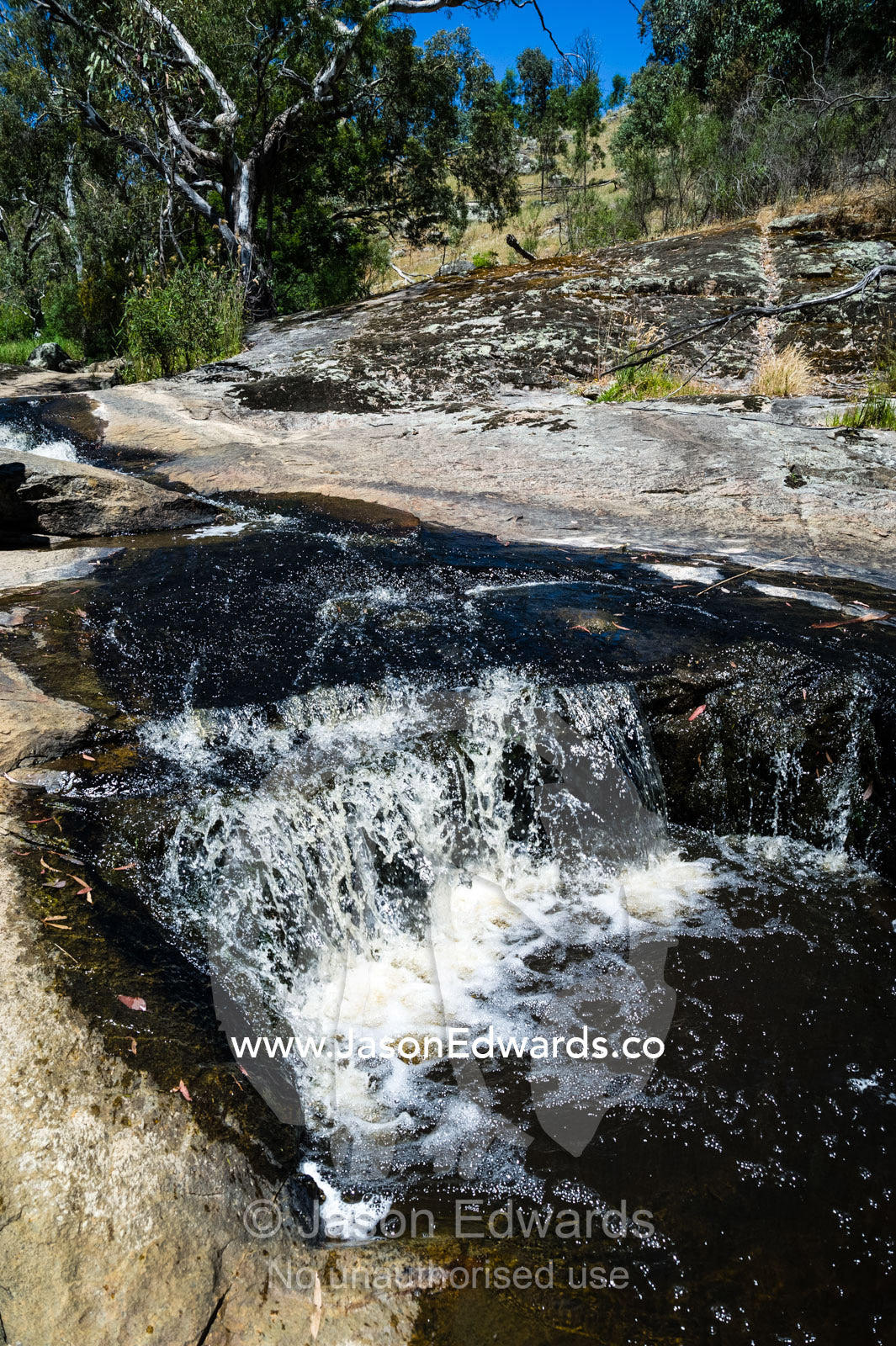 A stream cascades in a waterfall over boulders into a forest pool. Faithfuls Creek Waterfall, Euroa, Strathbogie, Victoria, Australia.