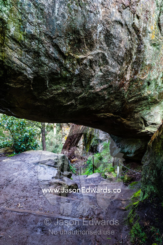 A rock pillar made of solvsbergite named the Hanging Rock is suspended over a walking trail. Hanging Rock Recreation Reserve, Woodend, Victoria, Australia.