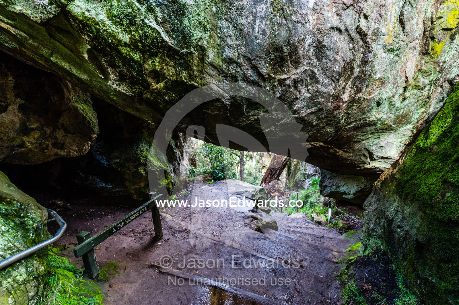 A rock pillar made of solvsbergite named the Hanging Rock is suspended over a walking trail. Hanging Rock Recreation Reserve, Woodend, Victoria, Australia.