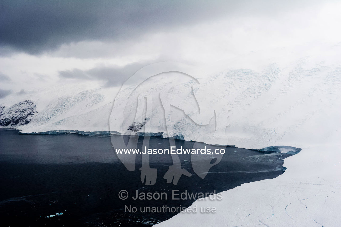 Cliffs covered in snow and ice tower above a dark ocean surface in an Antarctic bay. South West Face Mount Bird, Wohlschlag Bay, Ross Island, Antarctica.