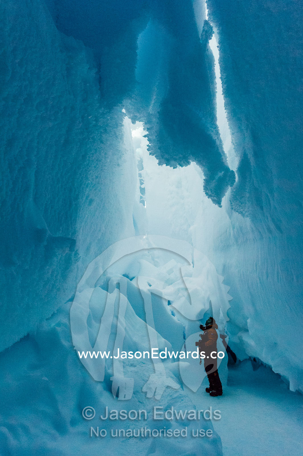 A photographer examines the frozen ceiling and icy walls of an ice cave in the Erebus Glacier Tongue. Erebus Ice Caves, Mount Erebus, Ross Island, Antarctica.