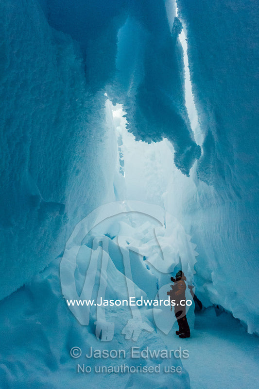 A photographer examines the frozen ceiling and icy walls of an ice cave in the Erebus Glacier Tongue. Erebus Ice Caves, Mount Erebus, Ross Island, Antarctica.