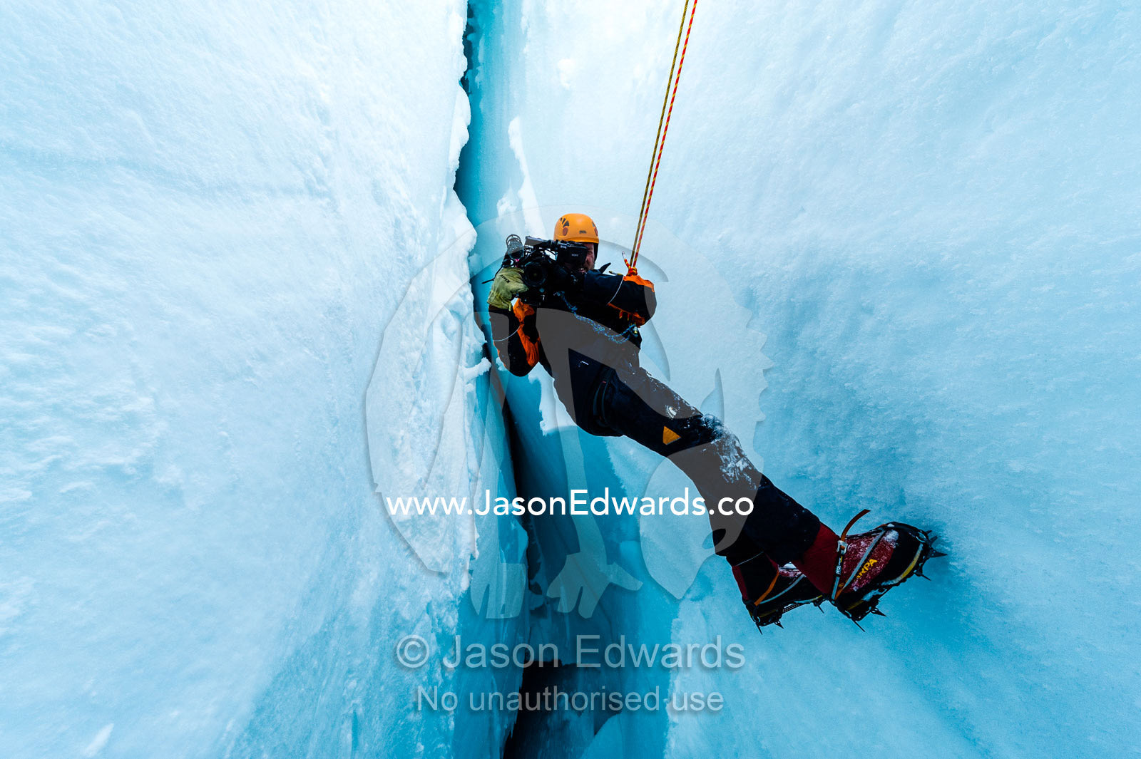 A cameraman filming from the sheer icy walls of a crevasse on the slopes of Mount Erebus in Antarctica. Silver City Ice Fall, Hut Point Peninsula, Ross Island Antarctica.