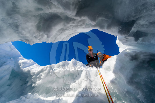 Ice guides peering into a crevasse on the slopes of Mount Erebus in Antarctica. Silver City Ice Fall, Hut Point Peninsula, Ross Island Antarctica.