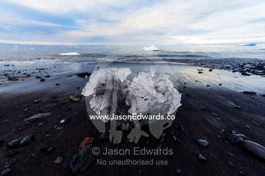 A boulder of glacier ice resting on a black volcanic beach in Antarctica. Caughley Beach, Cape Bird, Ross Island, Antarctica.