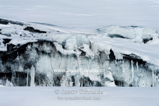 Icicles hang from the precipice of an ice cliff overlooking the sea ice. Turtle Rock, Erebus Bay, McMurdo Sound, Ross Island, Antarctica.