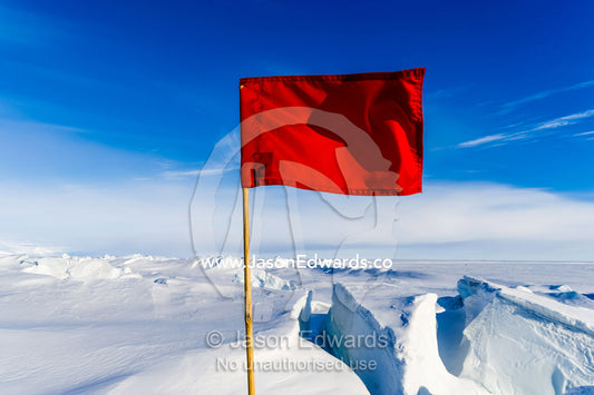 Bright red warning flags mark dangerous cracks and crevasse in the frozen sea ice. Pram Point, McMurdo Sound, Ross Island, Antarctica.