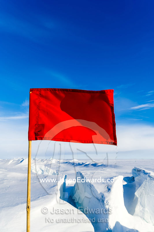 Bright red warning flags mark dangerous cracks and crevasse in the frozen sea ice. Pram Point, McMurdo Sound, Ross Island, Antarctica.