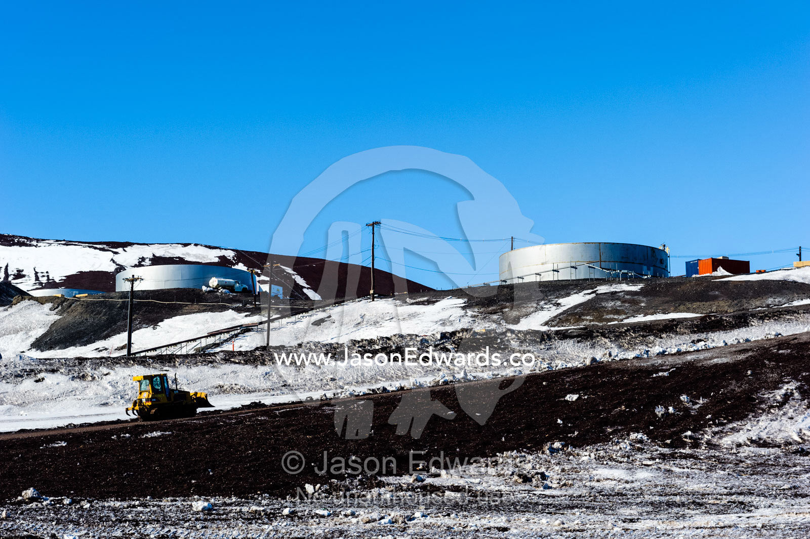 A tractor grader drives up a steep slope away from the construction of a wharf and dock. McMurdo Station, Ross Island, Antarctica.
