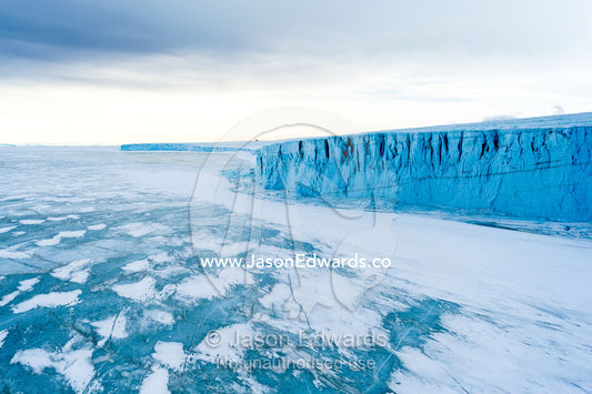 The sheer impregnable ice cliffs of a glacier tower over the frozen sea ice. Barne Glacier, Ross Sea, Ross Island, Antarctica.