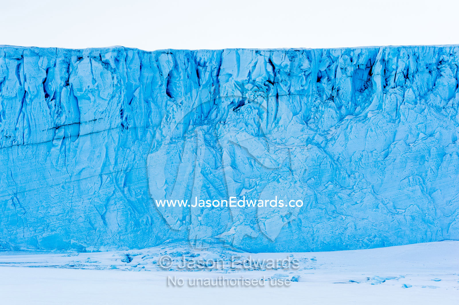 The sheer impregnable ice cliffs of a glacier tower over the frozen sea ice. Barne Glacier, Ross Sea, Ross Island, Antarctica.